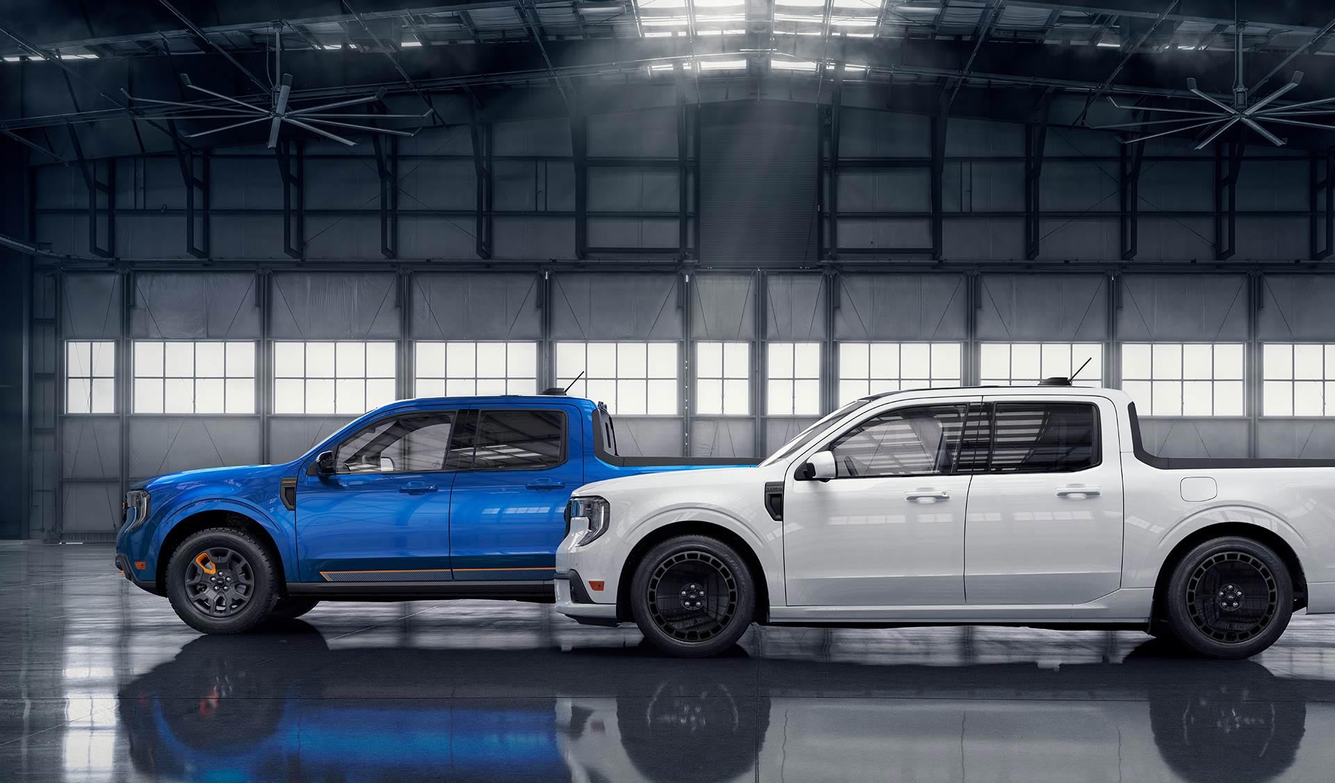 A white Ford Maverick Lobo pickup in front of a blue Ford Maverick TREMOR pickup, parked in an aircraft hangar.